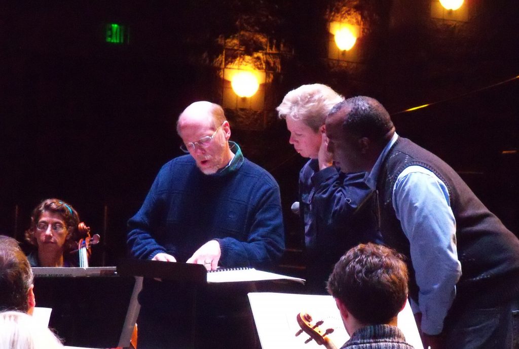 Rehearsal photo of composer Jesse Ayers with conductor Nan Washburn and narrator Emery Stephens